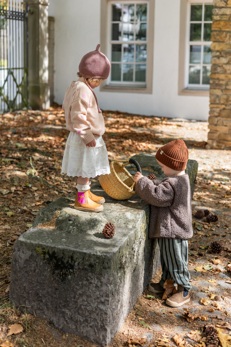 Two children on a fall morning, one wearing the Winter Janne Bootie in camel and star