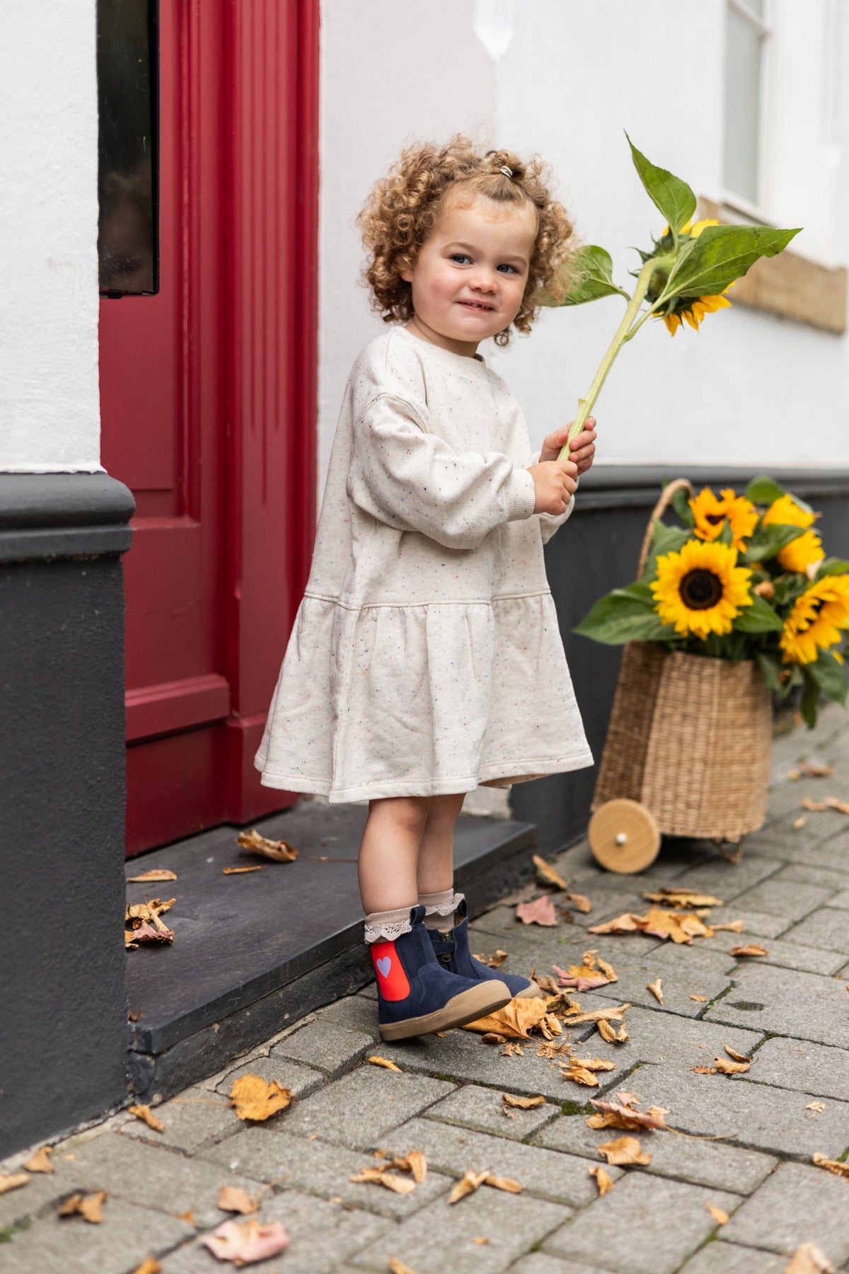Toddler holding a sunflower in navy Janne booties with a red heart panel