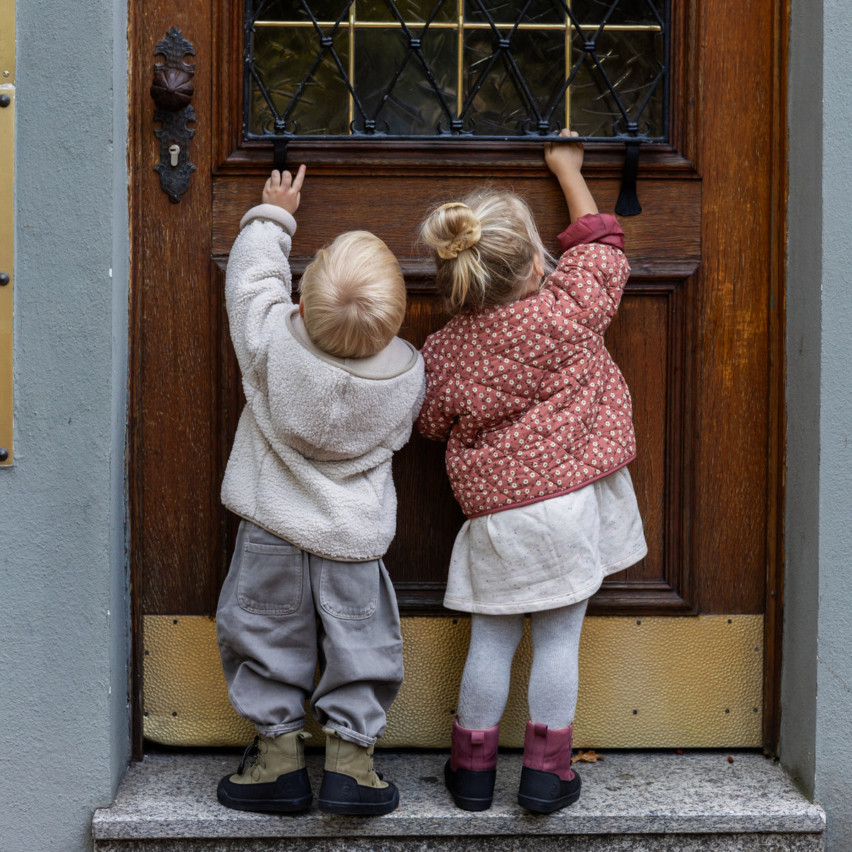 Two children at a front door, one wearing the First Step Finn in berry