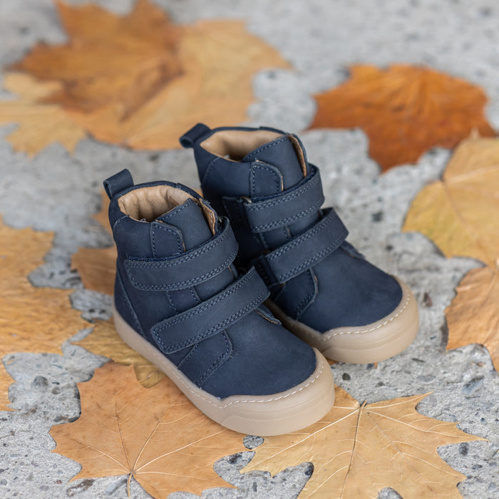 A pair of navy First Step Boots resting on fall leaves