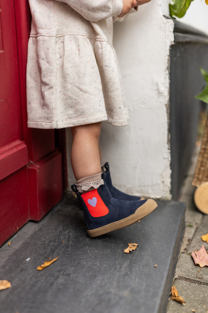Navy Janne bootie with a red heart panel, worn with a lace sock on a doorstep