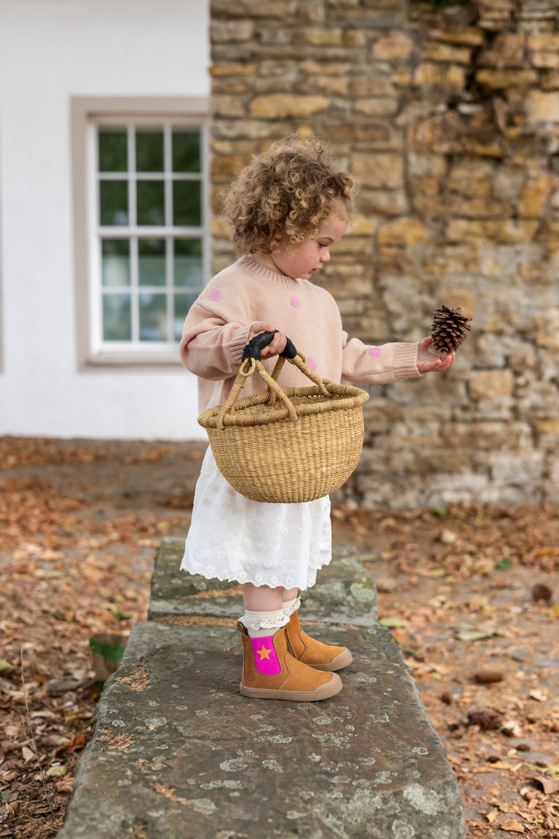 Toddler holding a pinecone in the Winter Janne Bootie in camel and star