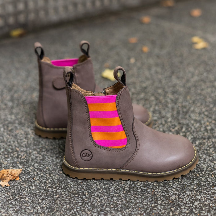 Pink and orange Chelsea boots resting on stone among fall leaves