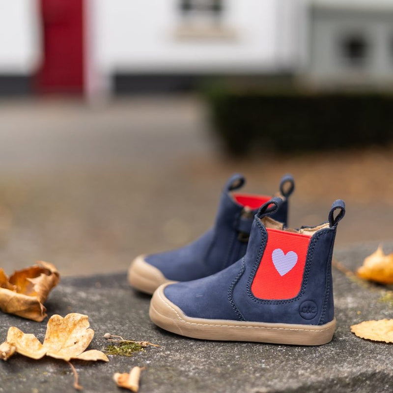 Navy Janne booties with a red heart panel among fall leaves